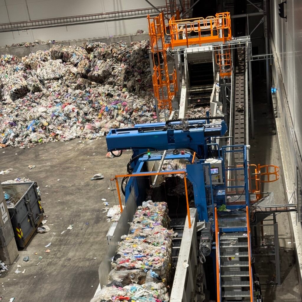 Kubene sendes innpå et transportbånd der en maskin klipper av ståltrådene som holder kubene sammen. Deretter går plastemballasjen videre inn i en kvern som åpner posene.